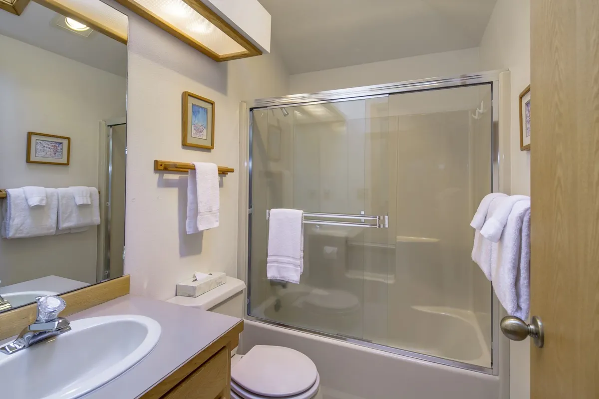 A serene bathroom scene with a glass-enclosed bathtub, neatly arranged towels, a bright sink area, and tasteful wall art. The space feels soothing and private, evoking a spa-like experience for guests.