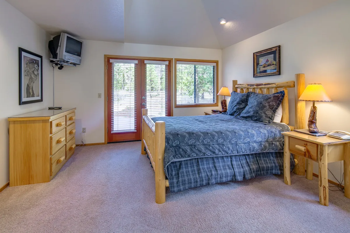 A tranquil bedroom featuring a queen bed with soft linens, French doors that invite natural light, a nightstand, a dresser, and tasteful artwork on the walls. The ambiance is calm, with a sense of privacy and relaxation, ideal for unwinding after a long day.