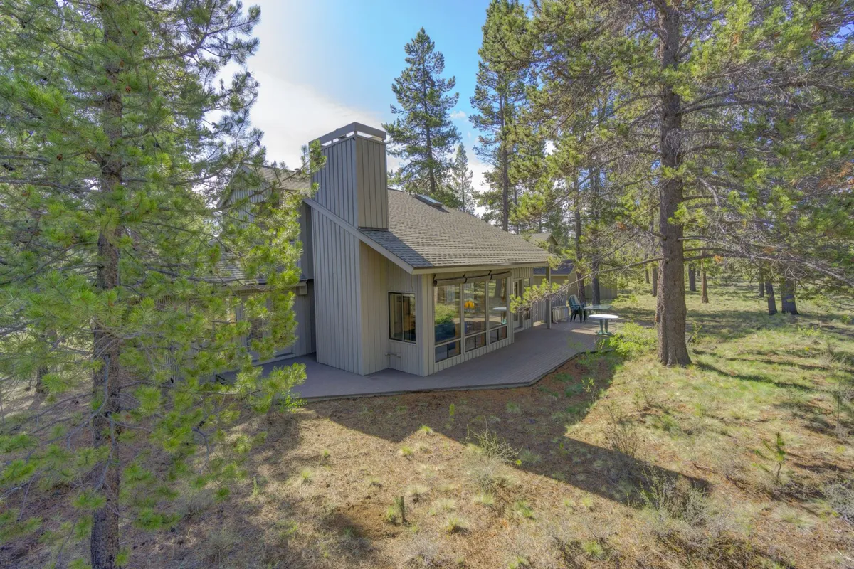 A tranquil exterior view of the home nestled among tall trees, with a spacious deck area ideal for gathering. The scene captures the connection between the house and the surrounding natural beauty, evoking a sense of adventure and relaxation.