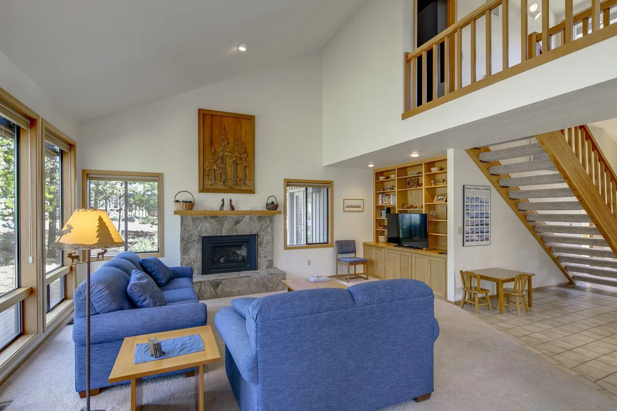 A warm, inviting living area featuring a glowing fireplace, plush sofa, wooden staircase, and tasteful artwork. The ambiance is both cozy and elegant, ideal for quiet evenings or sharing intimate moments by the fire.